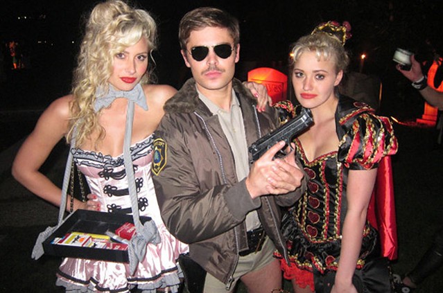 Zac Efron is ultra-serious as a retro cop with a big gun as he poses with duo Aly & AJ, both in racy costumes.