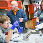 A professor conversing with two of his students as they complete a lab.