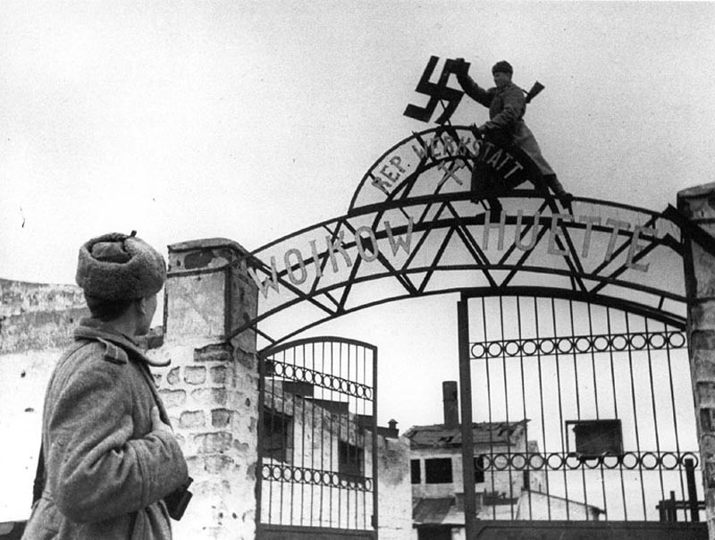 фото: Советский солдат срывает нацистскую свастику с ворот металлургического завода им. Войкова в освобождённой Керчи